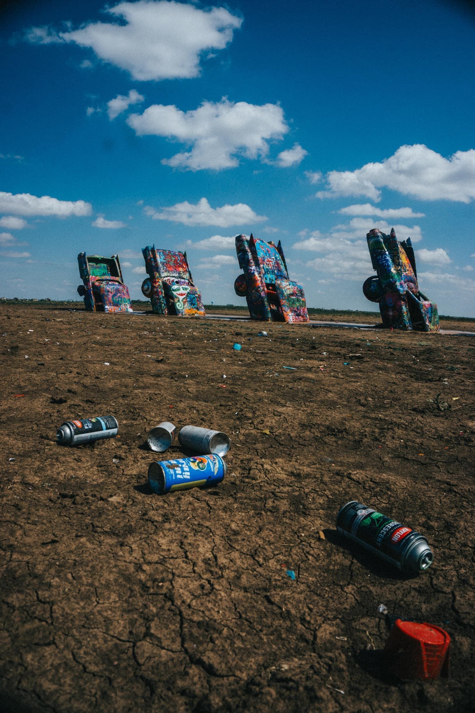 Des voitures recouvertes de graffitis, enfouies nez au sol dans un champ, des bombes de peinture vides jonchant la terre craquelée sous un ciel bleu et nuageux.