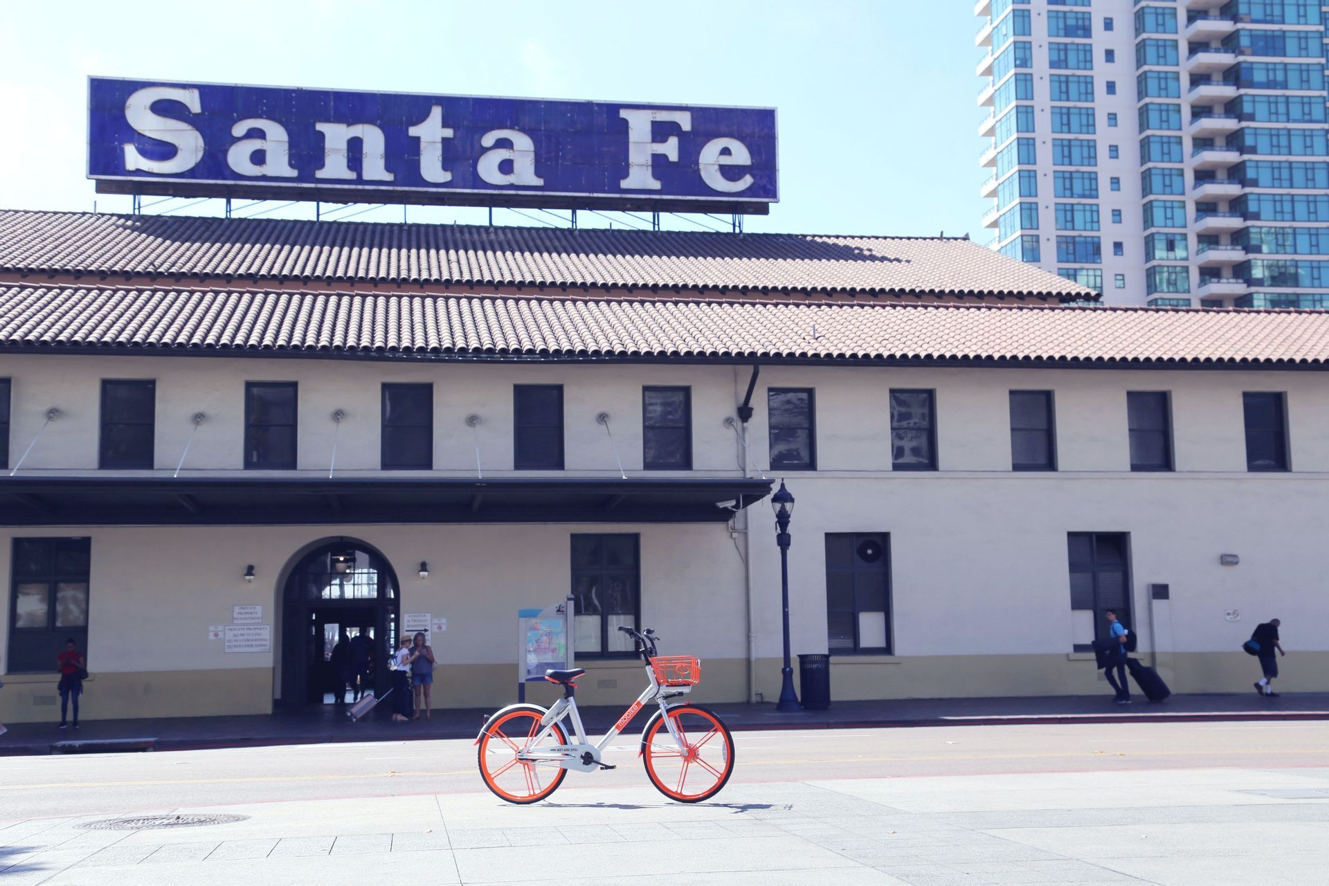 Un vélo orange et blanc est garé sur un trottoir de ville devant le bâtiment historique du Santa Fe Depot par une journée ensoleillée.