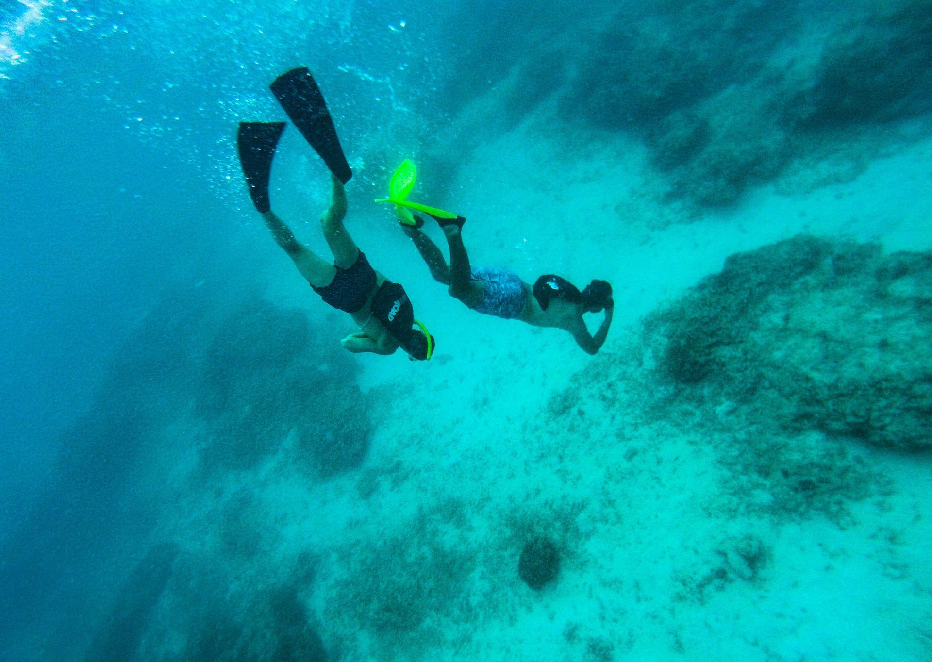 A WeRoad group trip with two people snorkeling in turquoise water above a rocky seafloor.