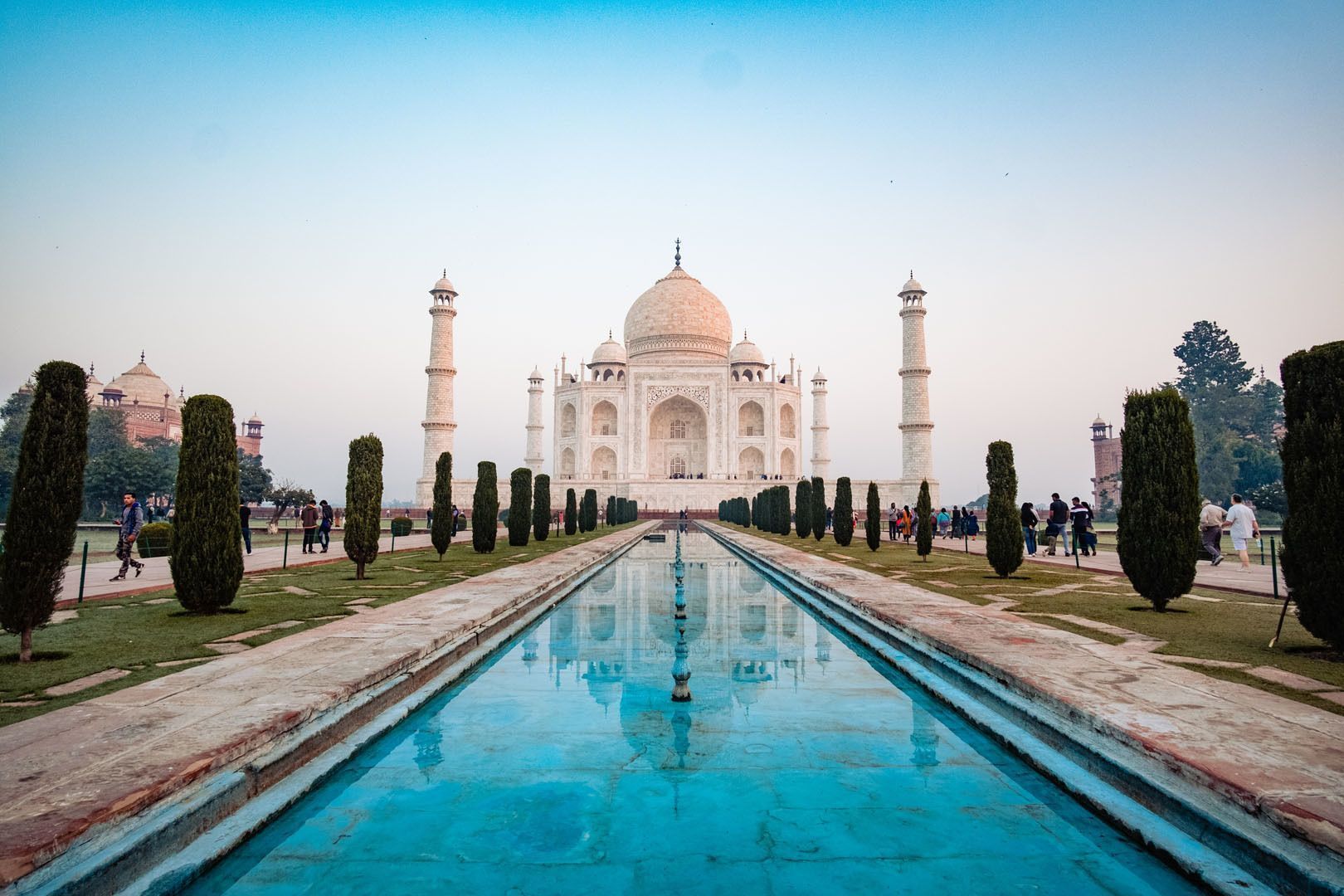 Le Taj Mahal se reflète dans un long bassin bordé de jardins de cyprès, avec des visiteurs se promenant sur les sentiers.