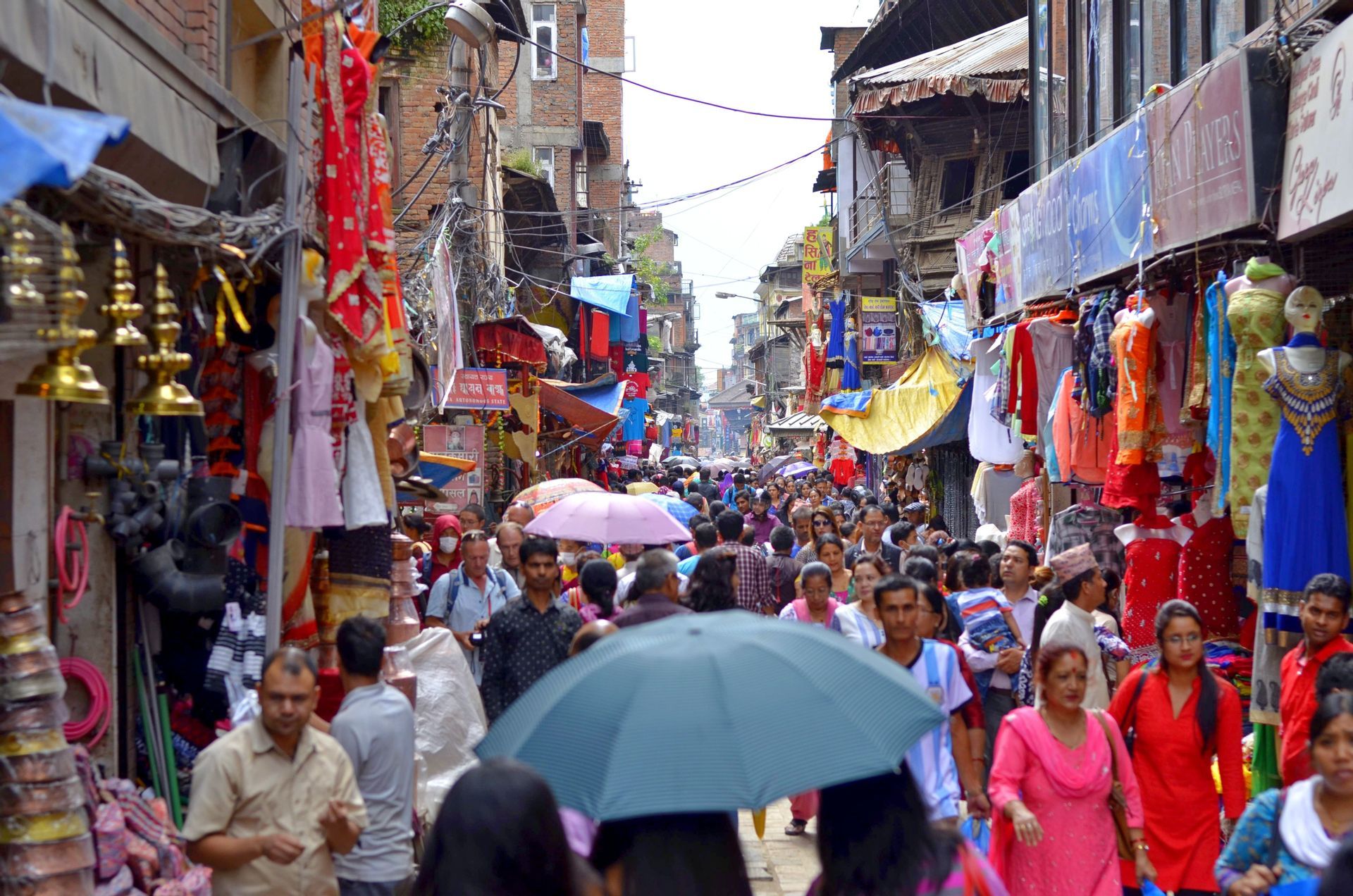 Une foule de gens marchant dans une rue de marché extérieur étroite et animée, bordée de boutiques et de marchandises colorées.