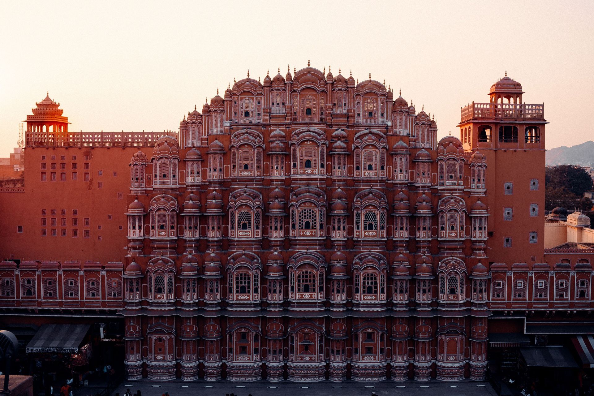 Una elaborada fachada de palacio de arenisca rosa con cientos de pequeñas ventanas de celosía bajo un cálido cielo de atardecer.