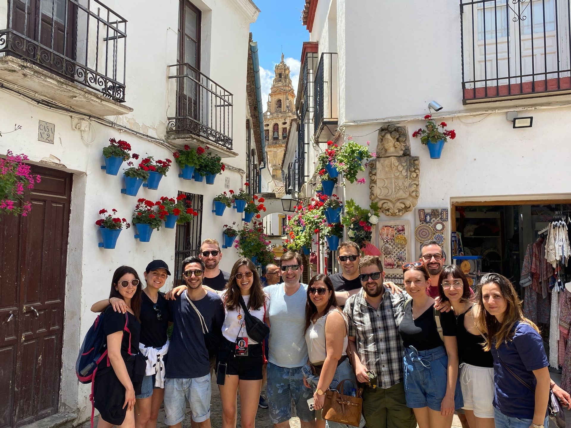 Un gruppo WeRoad in posa per una foto in una stretta via, fiancheggiata da edifici bianchi decorati con vasi di fiori blu.