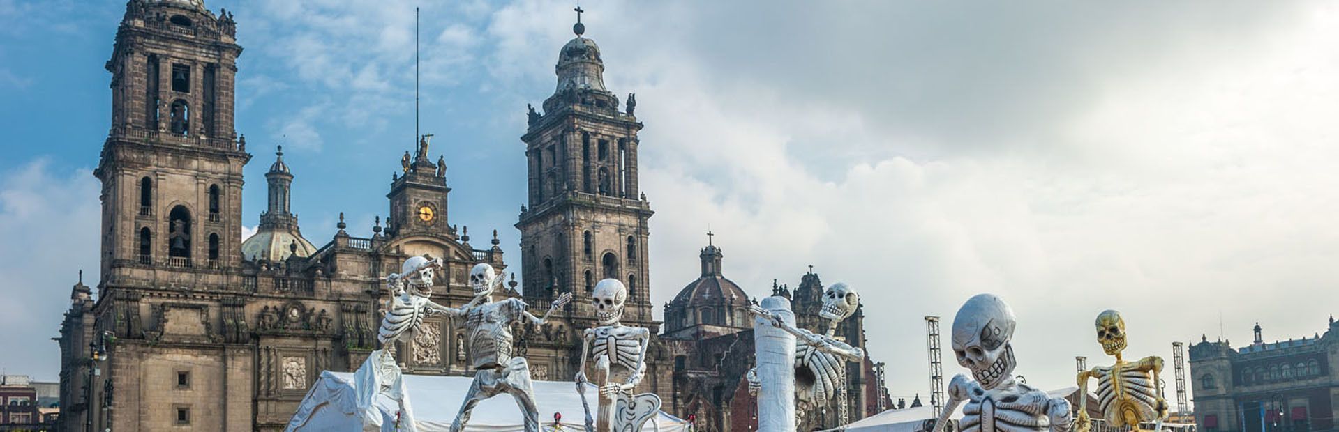 Grandes figuras de esqueletos para el festival del Día de Muertos están en exhibición frente a una catedral histórica.