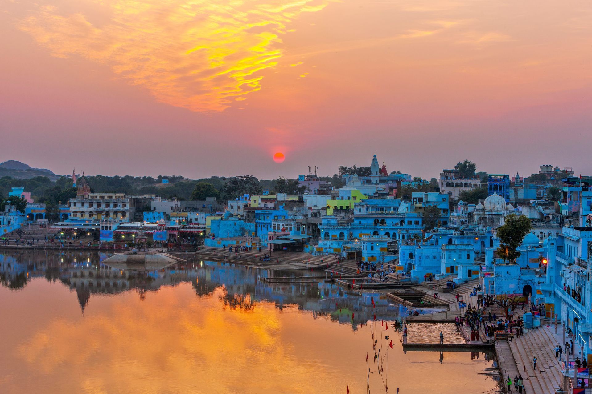 Una città di edifici blu costruita lungo la riva di un lago si riflette nell'acqua calma durante un tramonto vibrante.