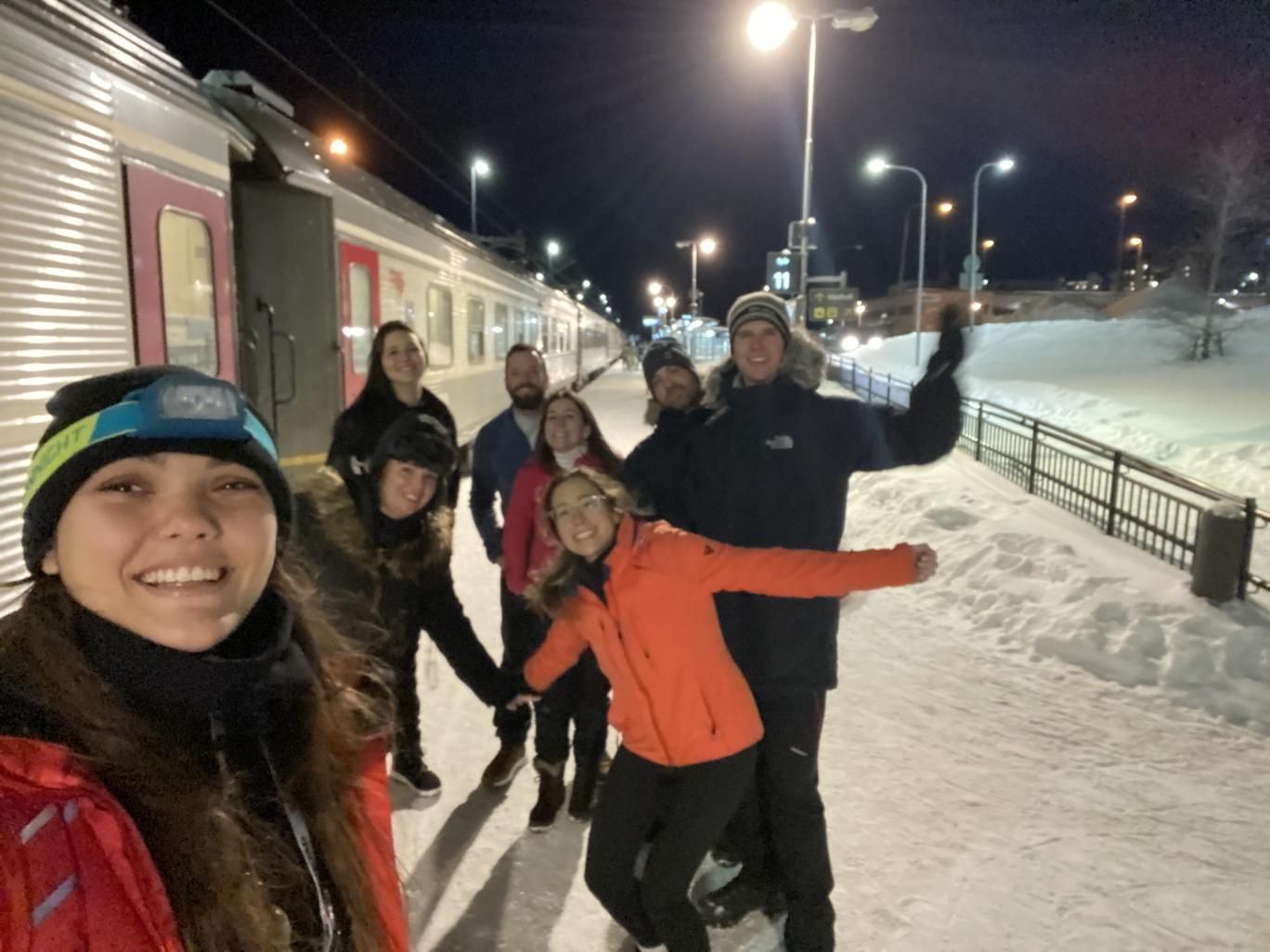 Un grupo de WeRoad se toma una selfie en una plataforma de tren nevada por la noche, de pie junto a un tren detenido.
