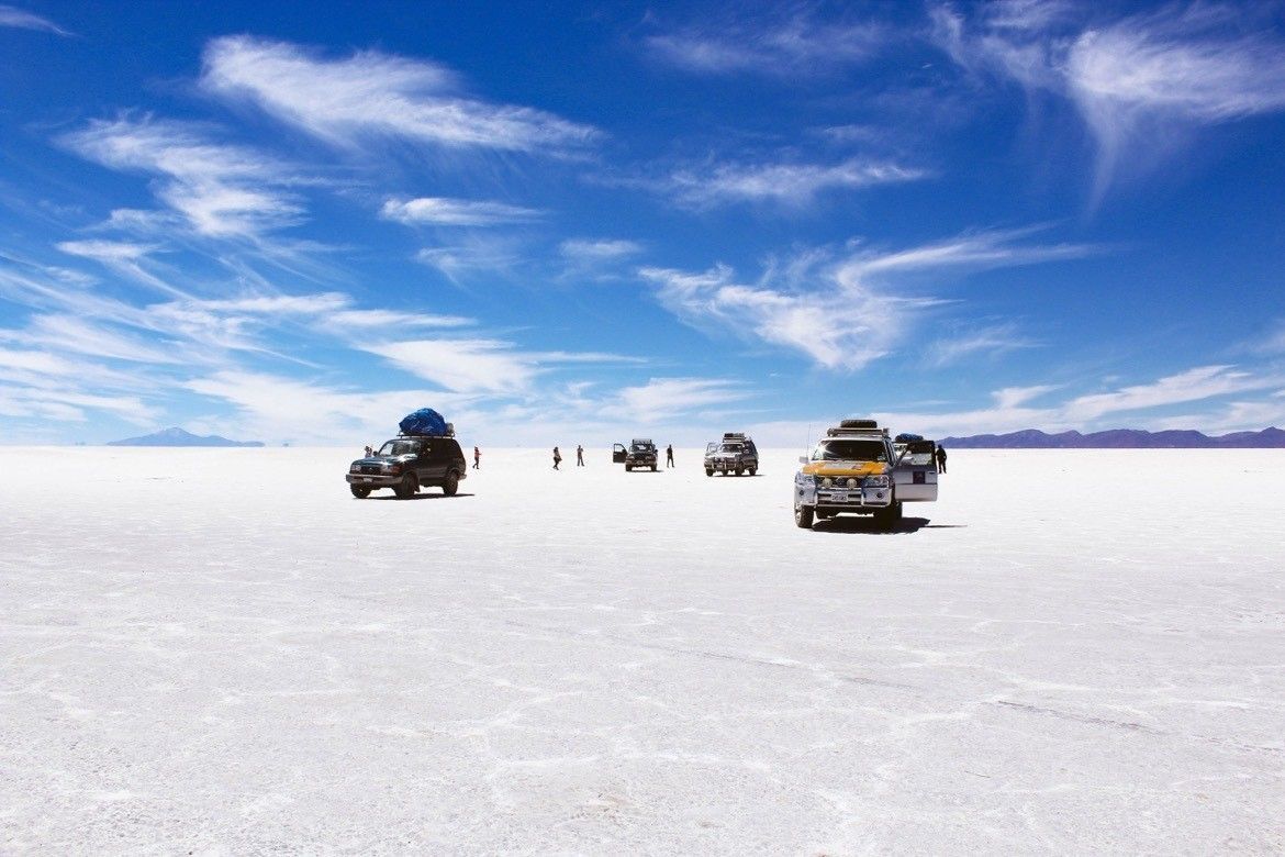 Eine WeRoad-Gruppenreise mit mehreren Geländefahrzeugen stoppte auf einer riesigen, weißen Salzebene unter einem strahlend blauen Himmel mit zarten Wolken.
