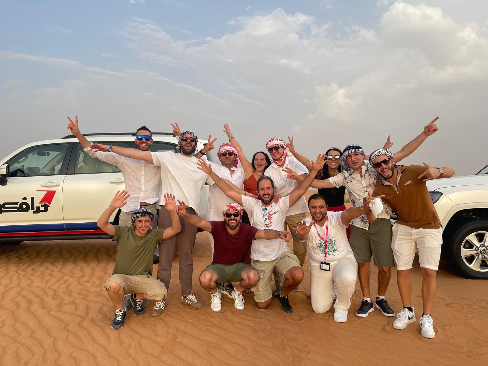 Un viaggio di gruppo WeRoad in posa mentre festeggiano insieme sulle dune di sabbia nel deserto vicino a un SUV