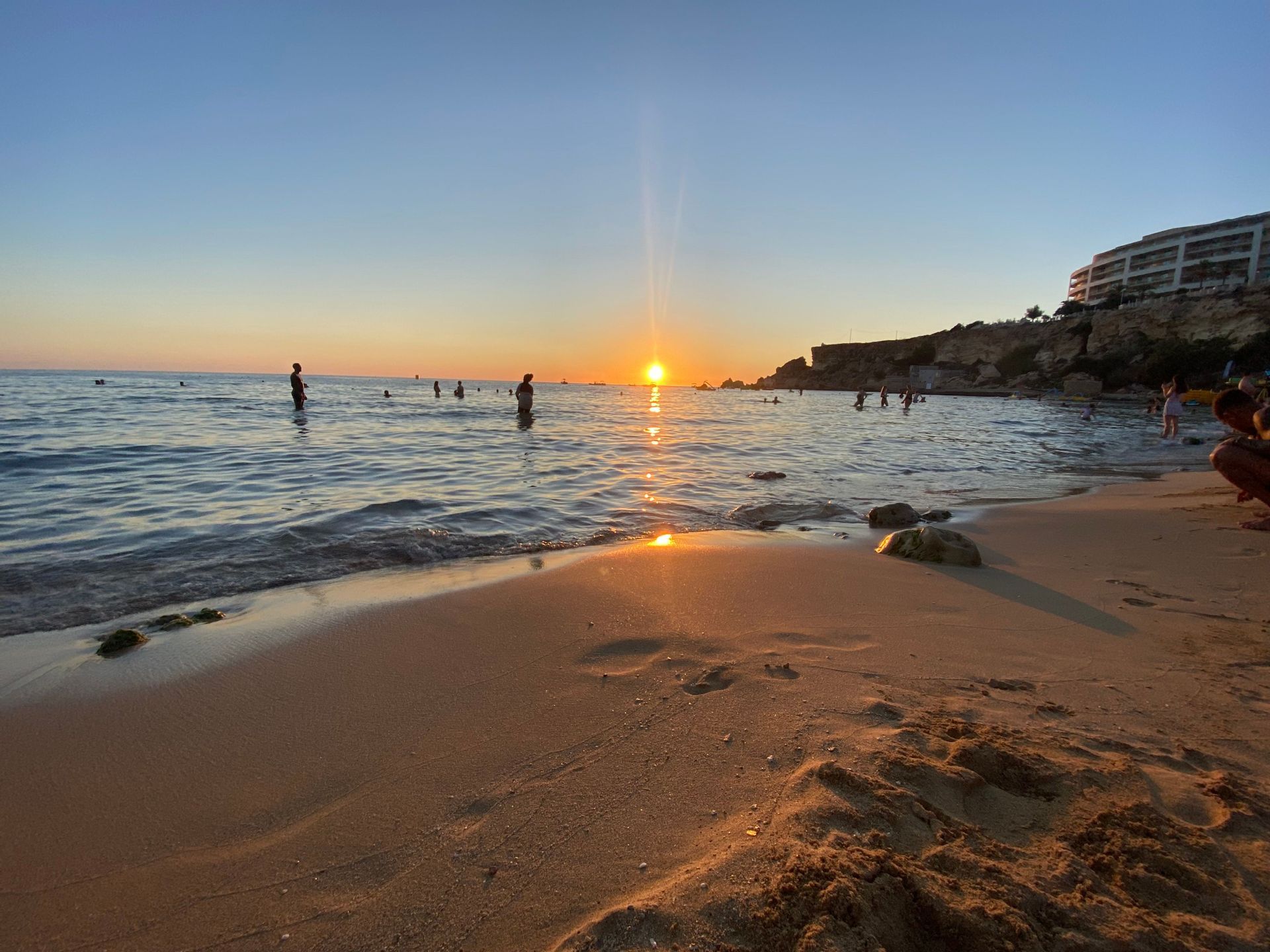 People swimming and relaxing in the sea along a sandy beach during sunset.