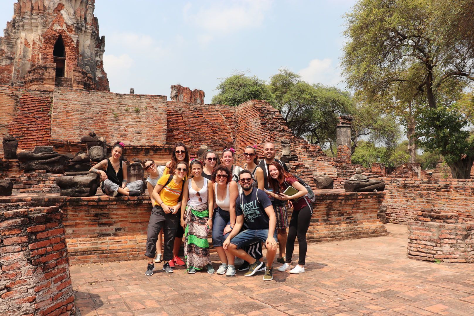 Un groupe WeRoad en voyage sourit et pose pour une photo au milieu de ruines de temples anciens en briques rouges, sous un ciel dégagé.
