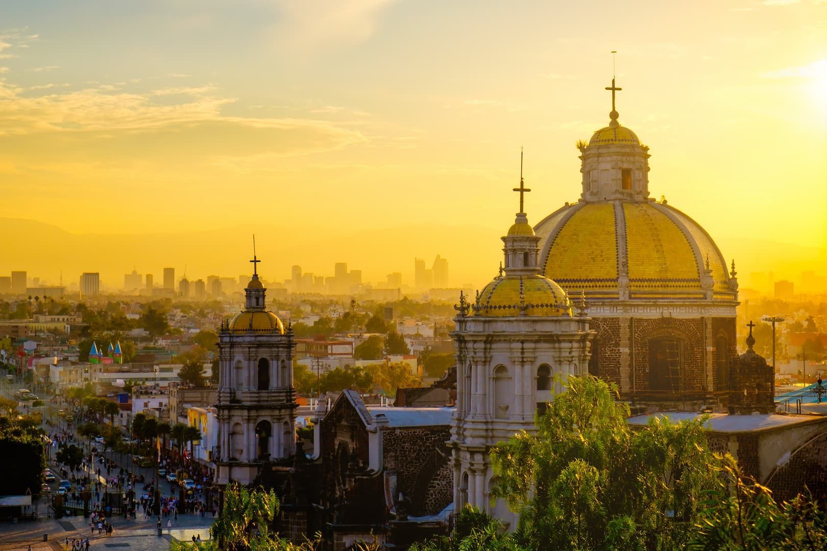 Una catedral histórica con cúpulas doradas con vistas a una ciudad con un horizonte moderno durante un atardecer dorado.