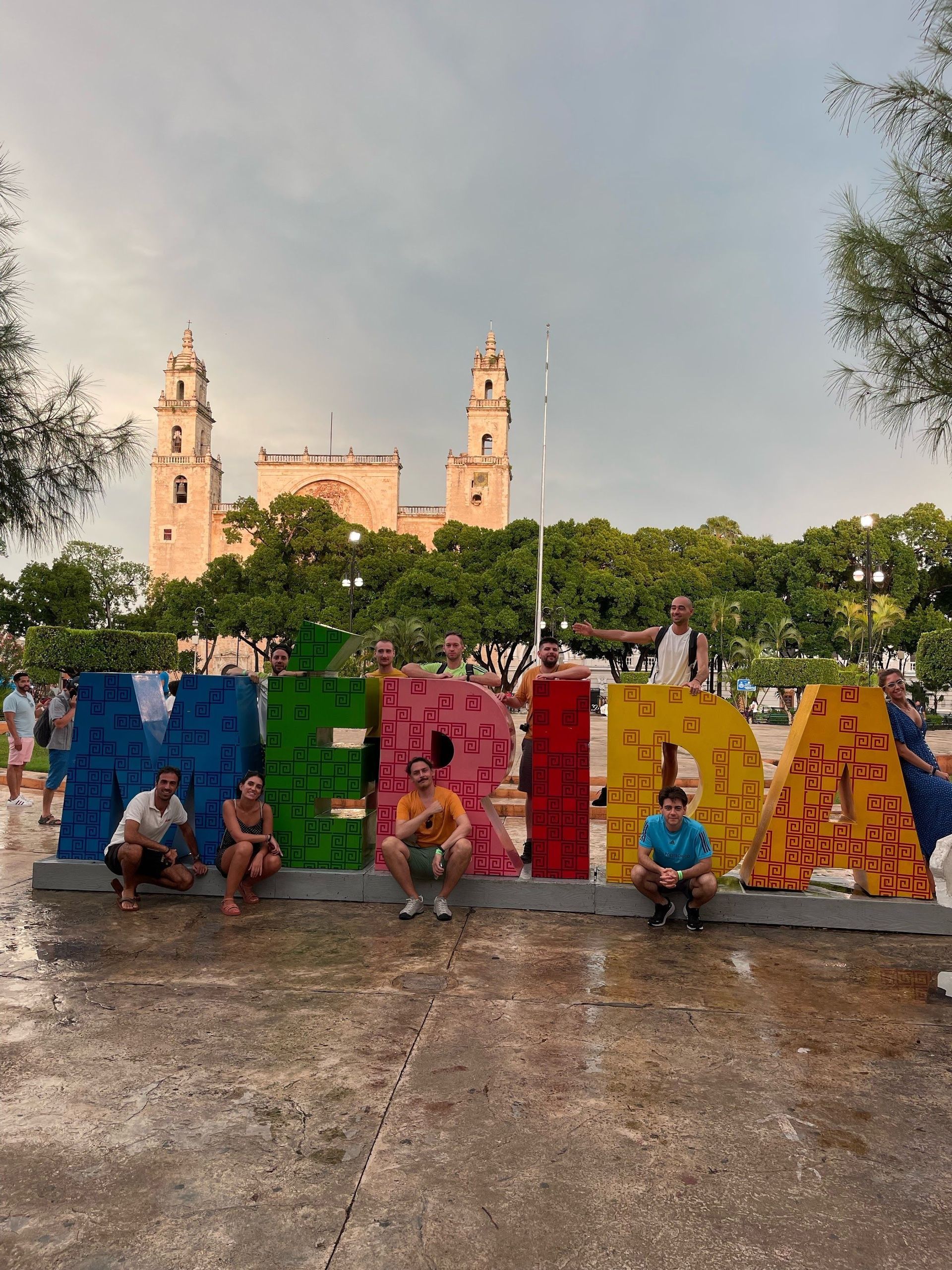 Eine WeRoad-Gruppe posiert für ein Foto vor den großen, farbenfrohen MERIDA-Buchstaben auf einem Platz mit Kathedrale im Hintergrund.