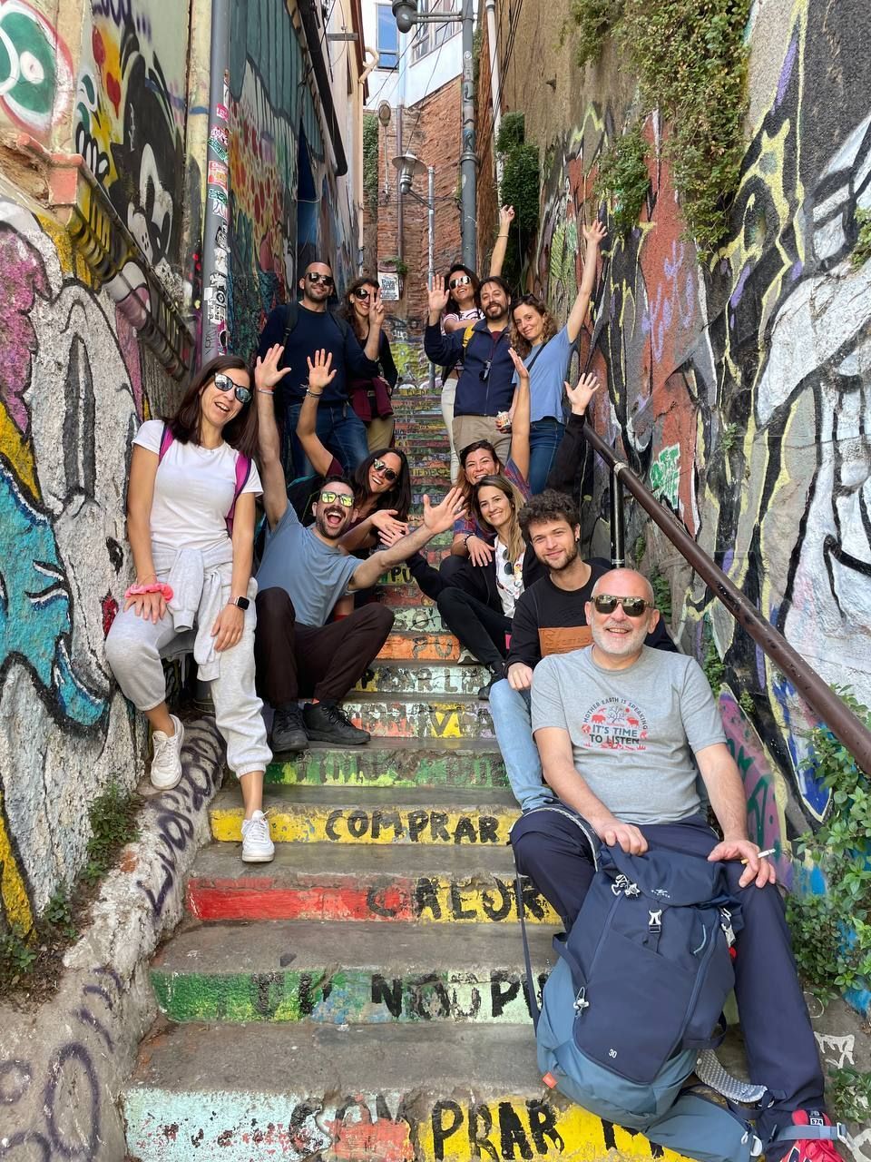 A WeRoad group trip posing for a photo on a colorful outdoor staircase surrounded by walls covered in graffiti.