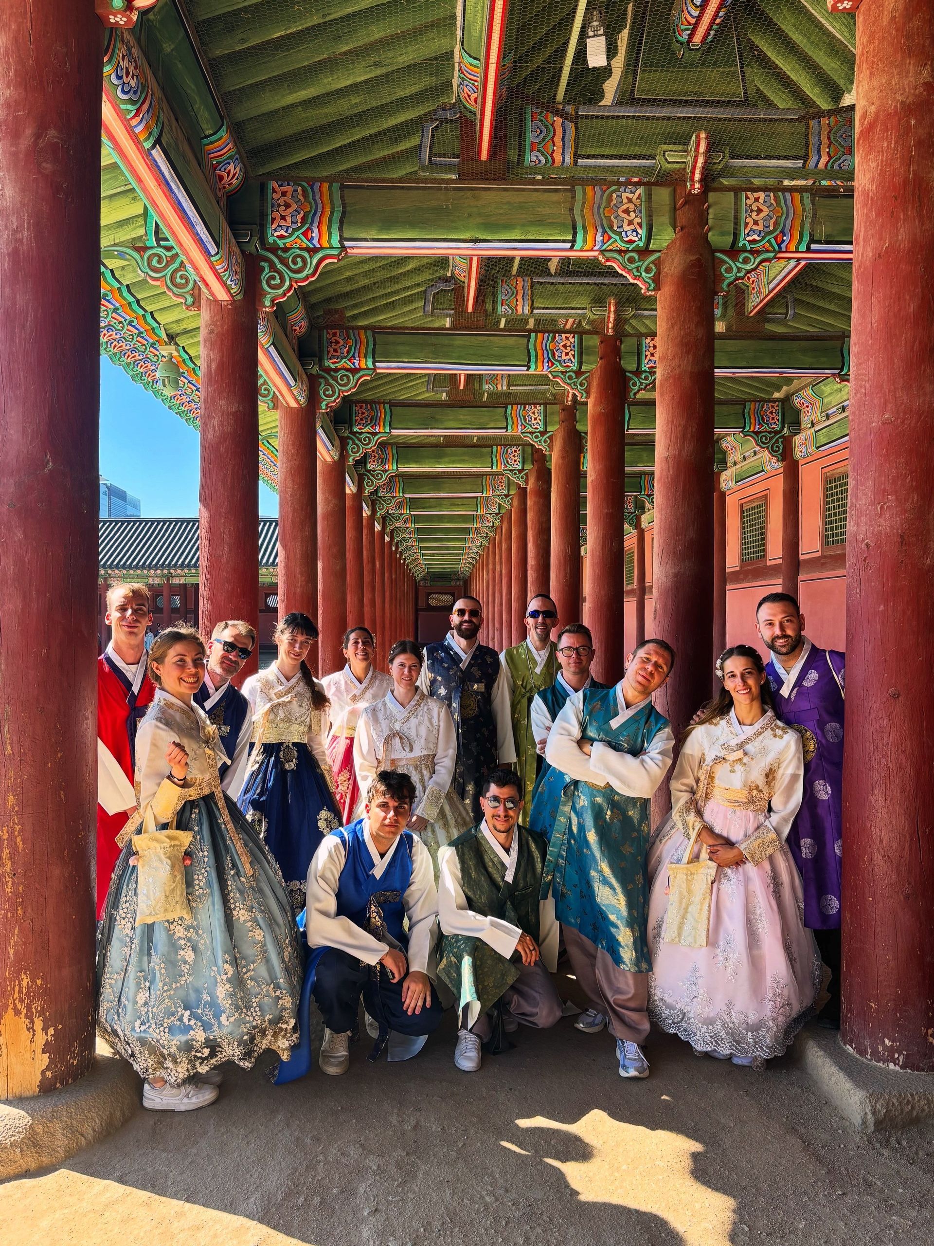 Un groupe de voyage WeRoad posant ensemble en vêtements traditionnels sous une colonnade historique couverte.
