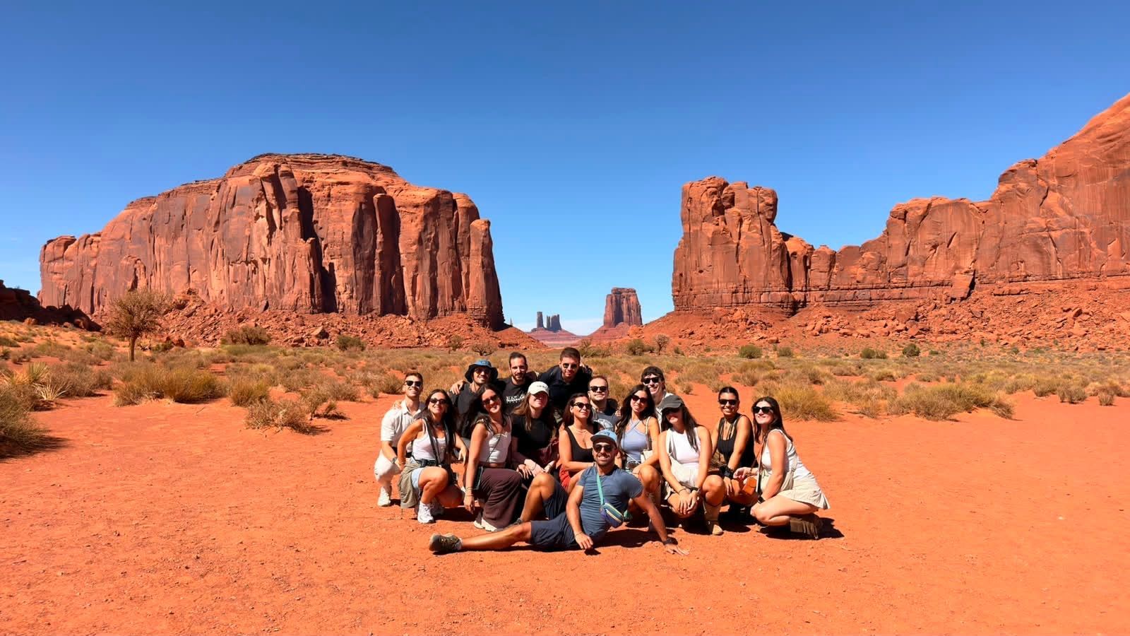 Un viaggio di gruppo WeRoad in posa insieme in un paesaggio desertico con grandi formazioni di roccia rossa sotto un cielo azzurro e limpido