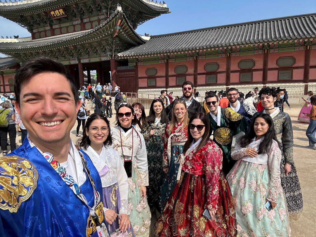 Un viaje en grupo WeRoad, vistiendo ropa tradicional coreana, posa para una selfie grupal frente a un edificio histórico.