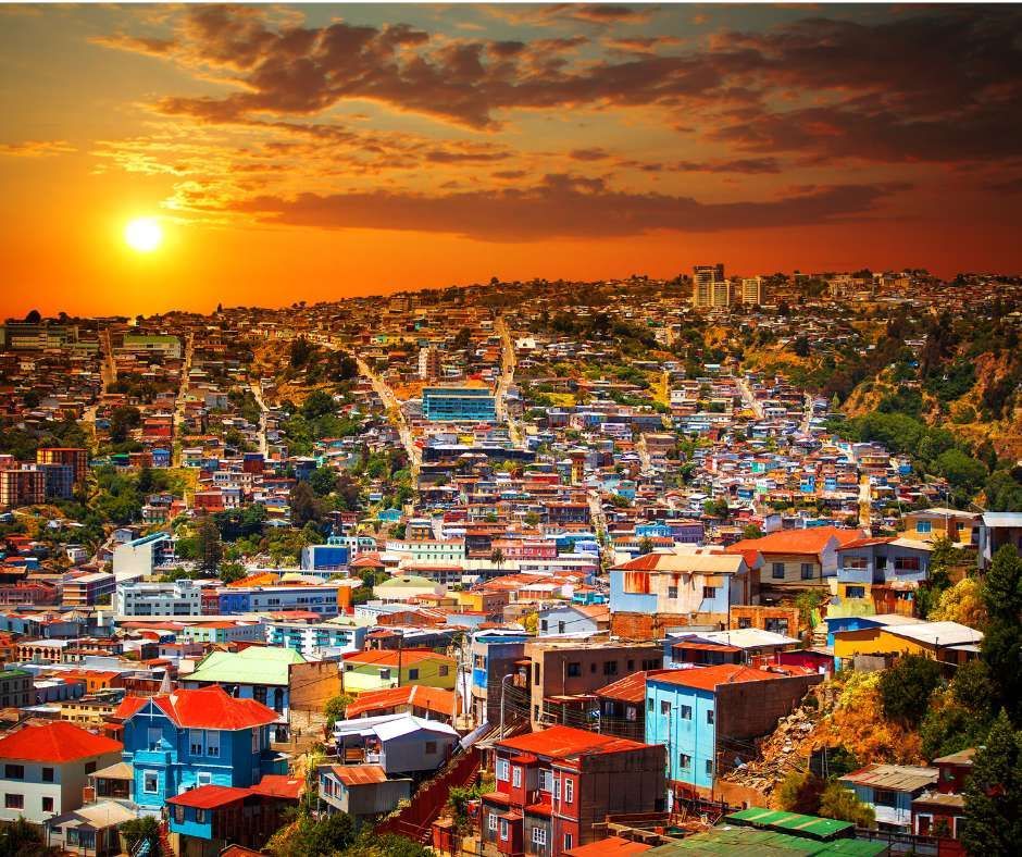 Une dense collection de bâtiments colorés s'étend sur une colline sous un ciel de coucher de soleil orangé.