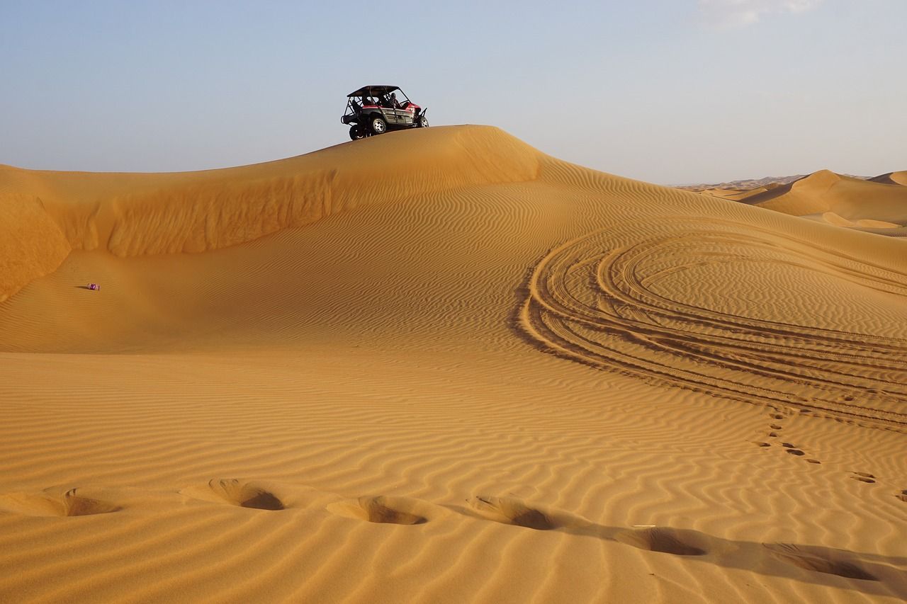A dune buggy from a WeRoad group trip sits atop a sand dune, with tire tracks and footprints marking the desert landscape.
