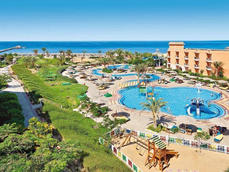 Una vista aerea di un grande resort balneare con una piscina, un parco giochi per bambini e una spiaggia sabbiosa accanto all'oceano.