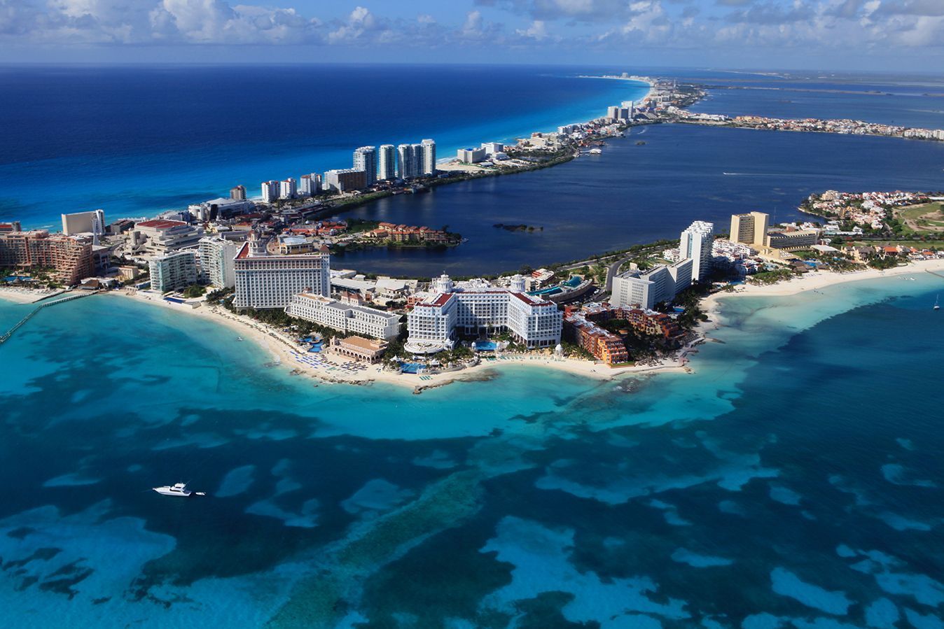 Aerial view of a coastal city with hotels lining a white sand beach, bordered by turquoise and deep blue ocean waters.