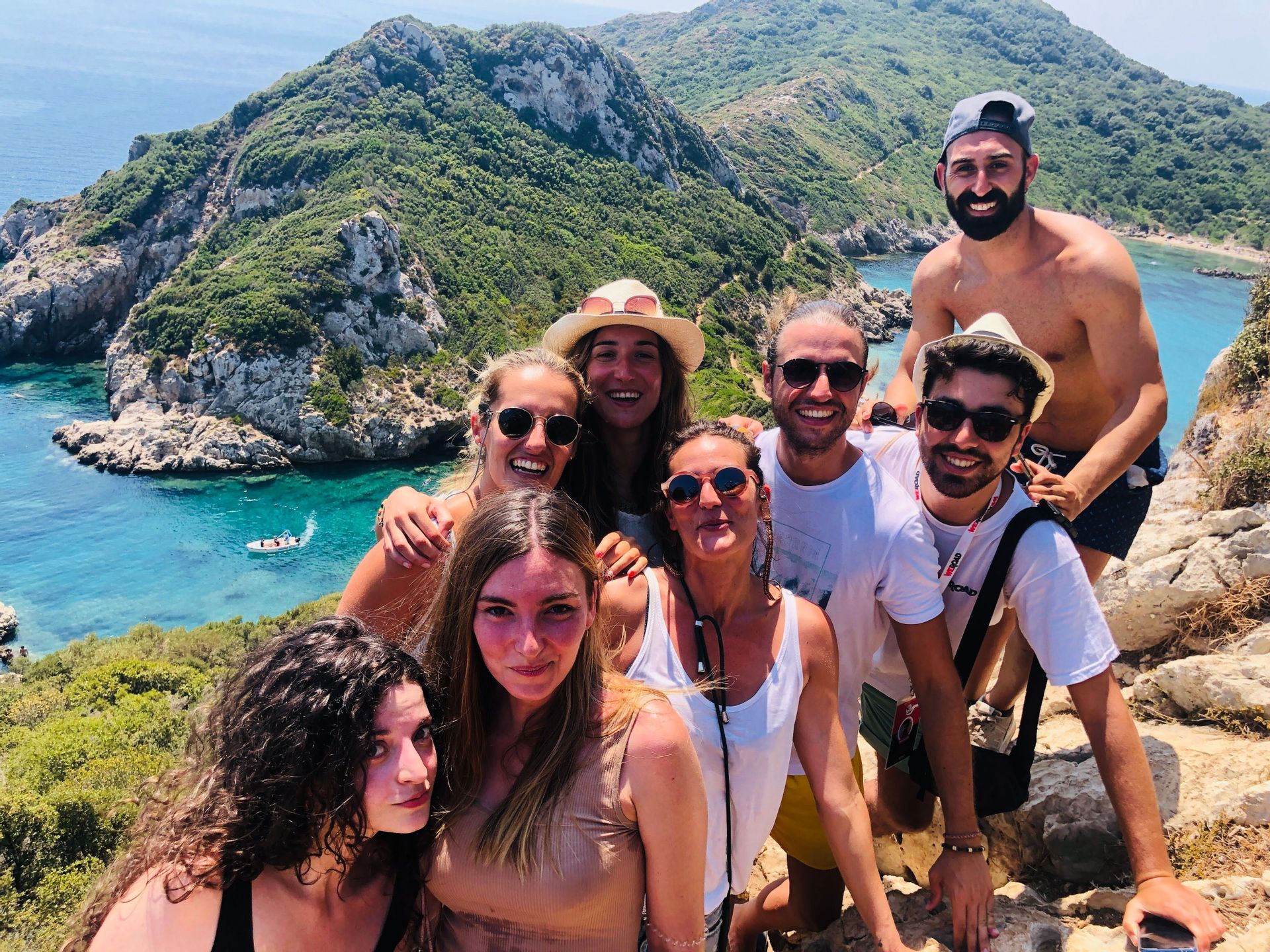 Un grupo de WeRoad sonríe para una selfie en un acantilado con vistas a una bahía turquesa y exuberantes colinas verdes.