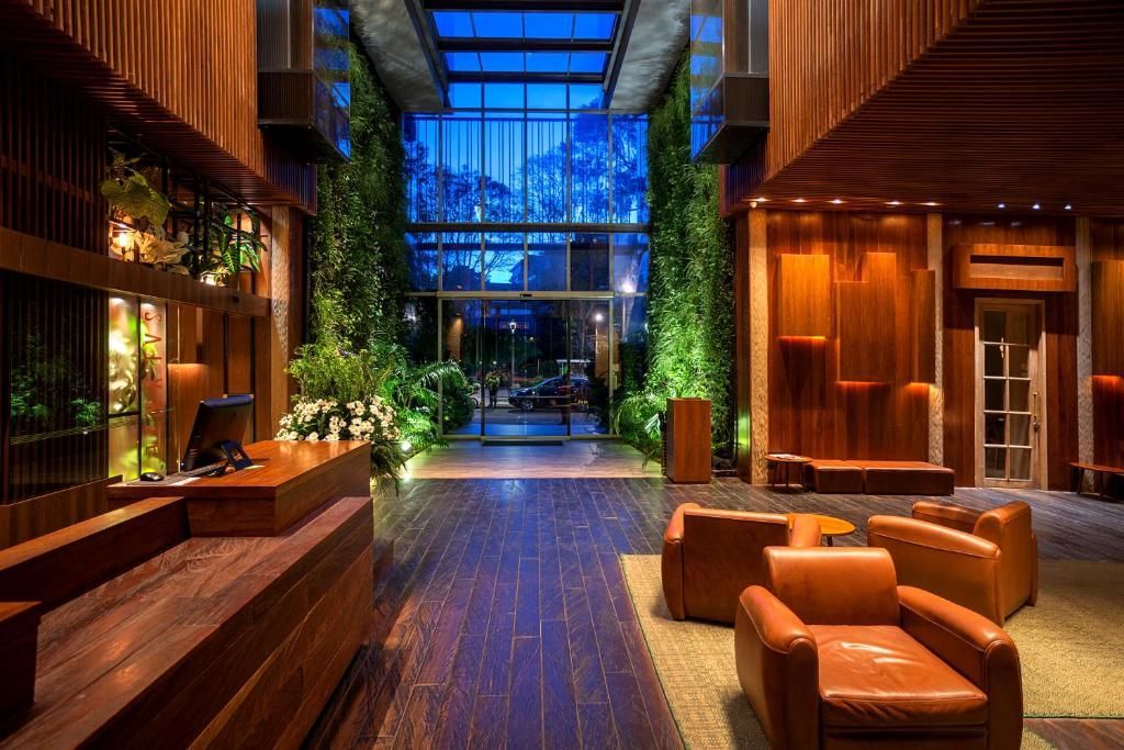 The lobby of a modern hotel featuring wood paneling, illuminated vertical gardens, and a seating area with leather armchairs.