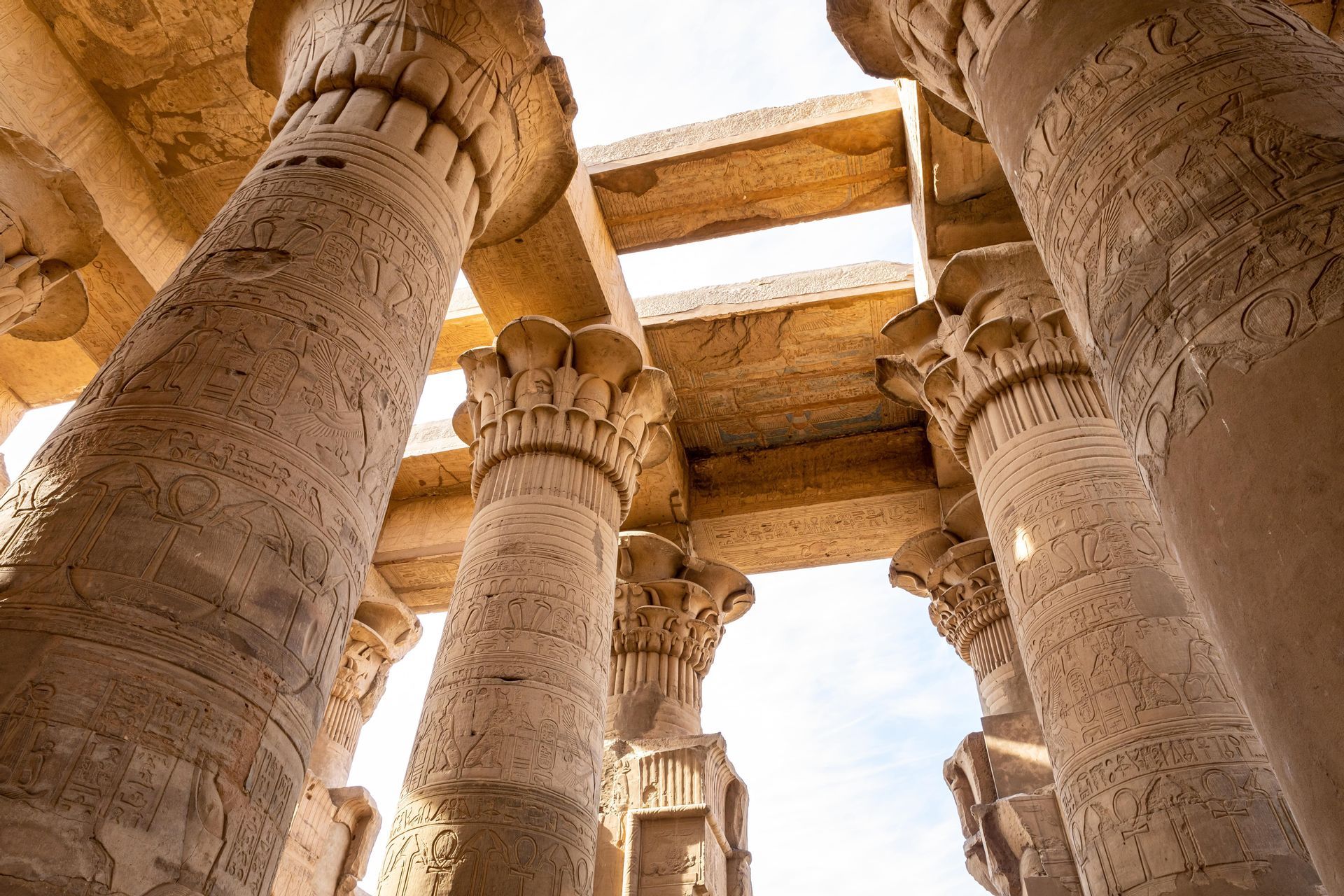 Una vista dal basso di grandi colonne di pietra con geroglifici scolpiti all'interno di un antico tempio, che sorreggono un soffitto di pietra.