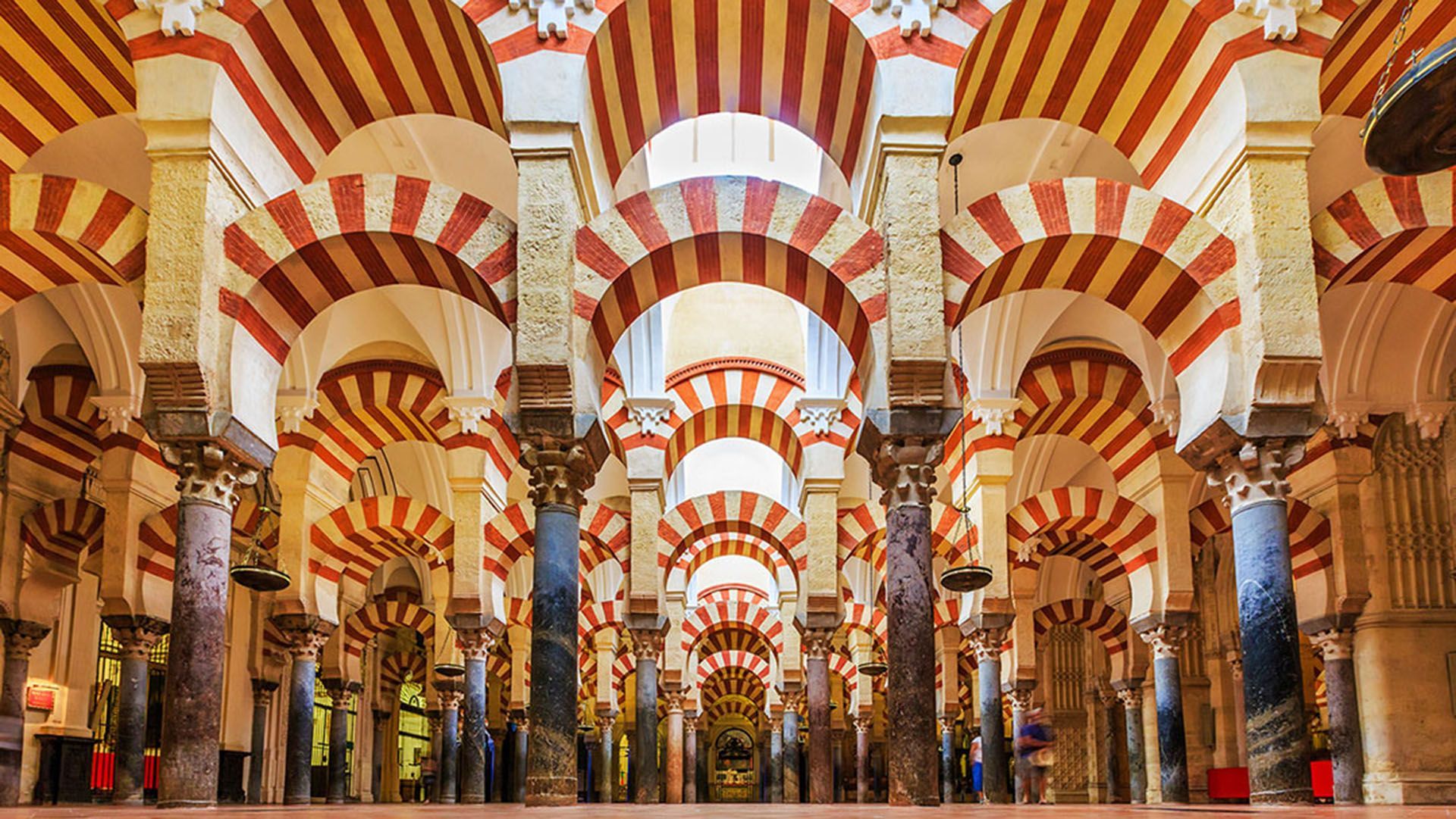 Interior view of a hall with rows of columns supporting distinctive red and beige striped double arches.