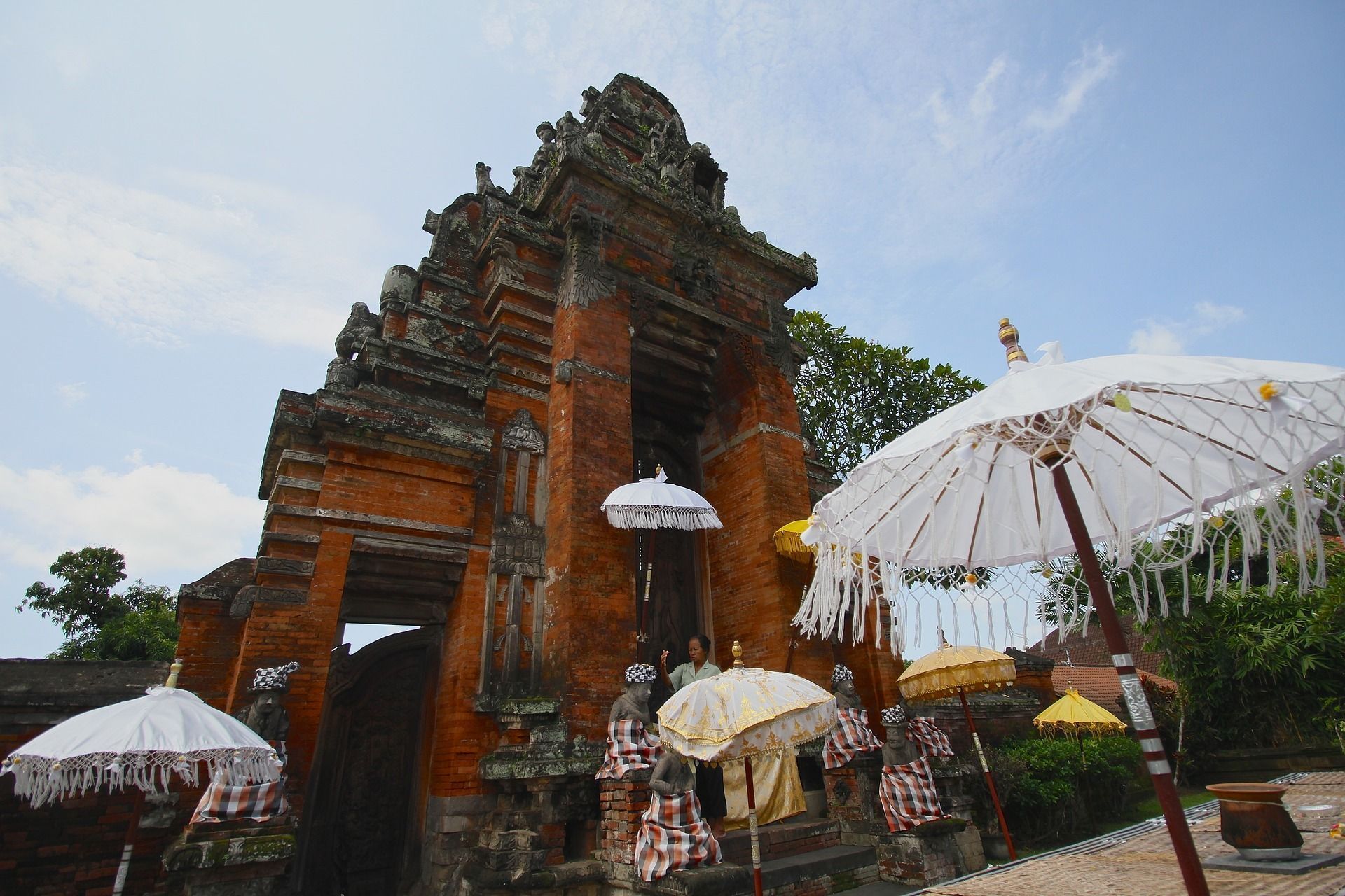 A low-angle view of an ornate, multi-tiered brick temple entrance decorated with traditional white and yellow umbrellas.