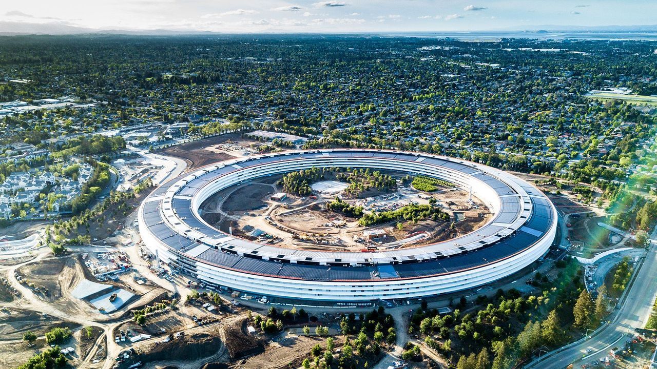Veduta aerea di un imponente edificio circolare in costruzione, immerso in un ampio paesaggio suburbano verde.