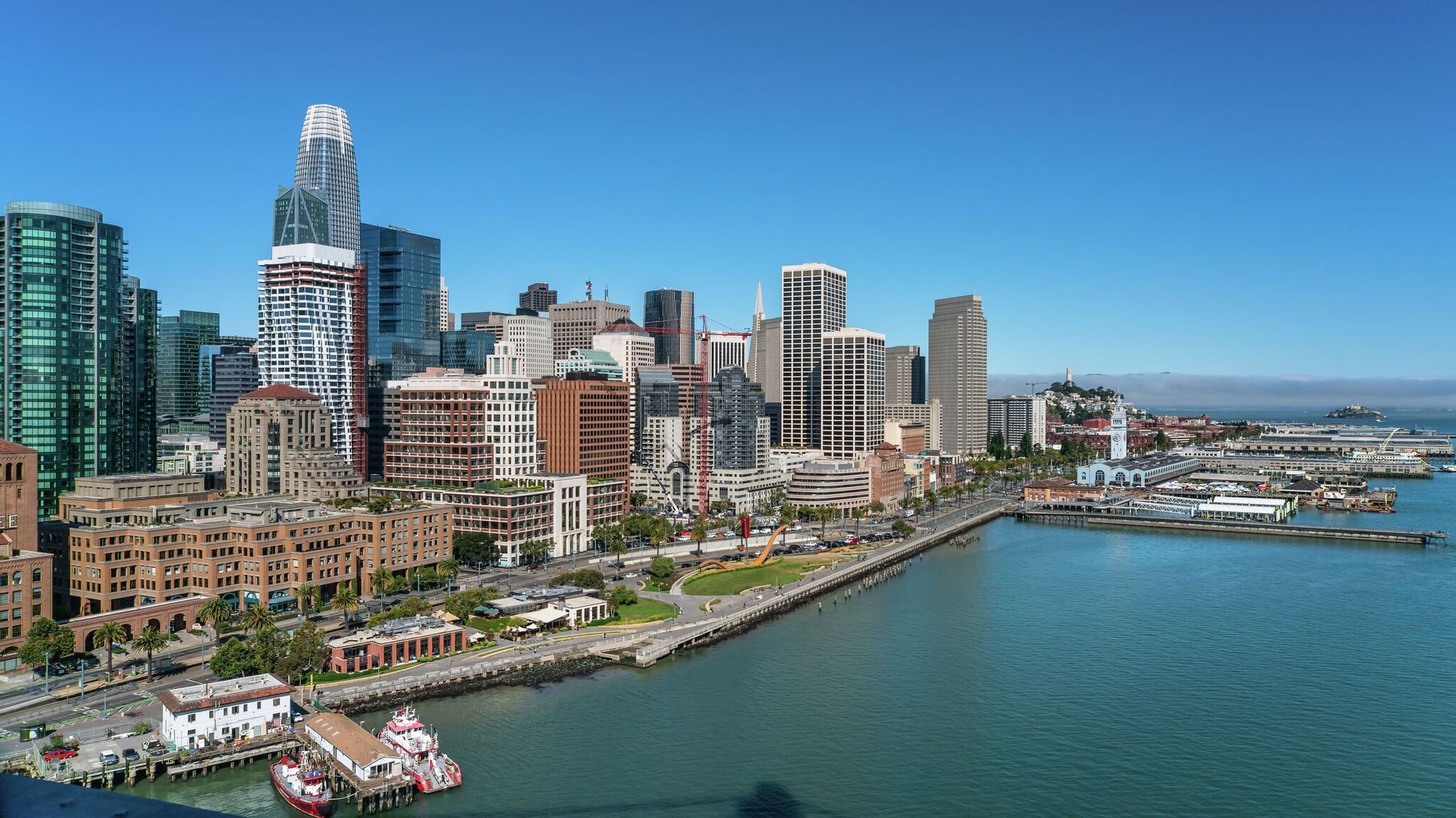Vista panoramica dello skyline di una città moderna con alti grattacieli che si affacciano su una baia calma sotto un cielo azzurro.