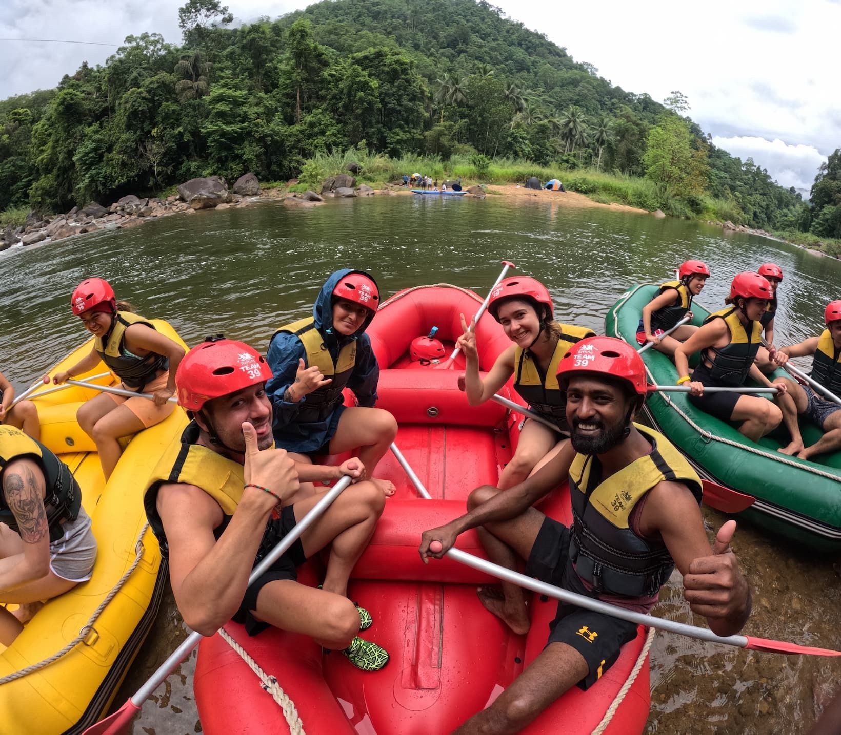 Un gruppo WeRoad in viaggio posa per una foto su gommoni gonfiabili su un fiume, indossando caschi rossi e giubbotti di salvataggio, con una collina boscosa alle spalle.