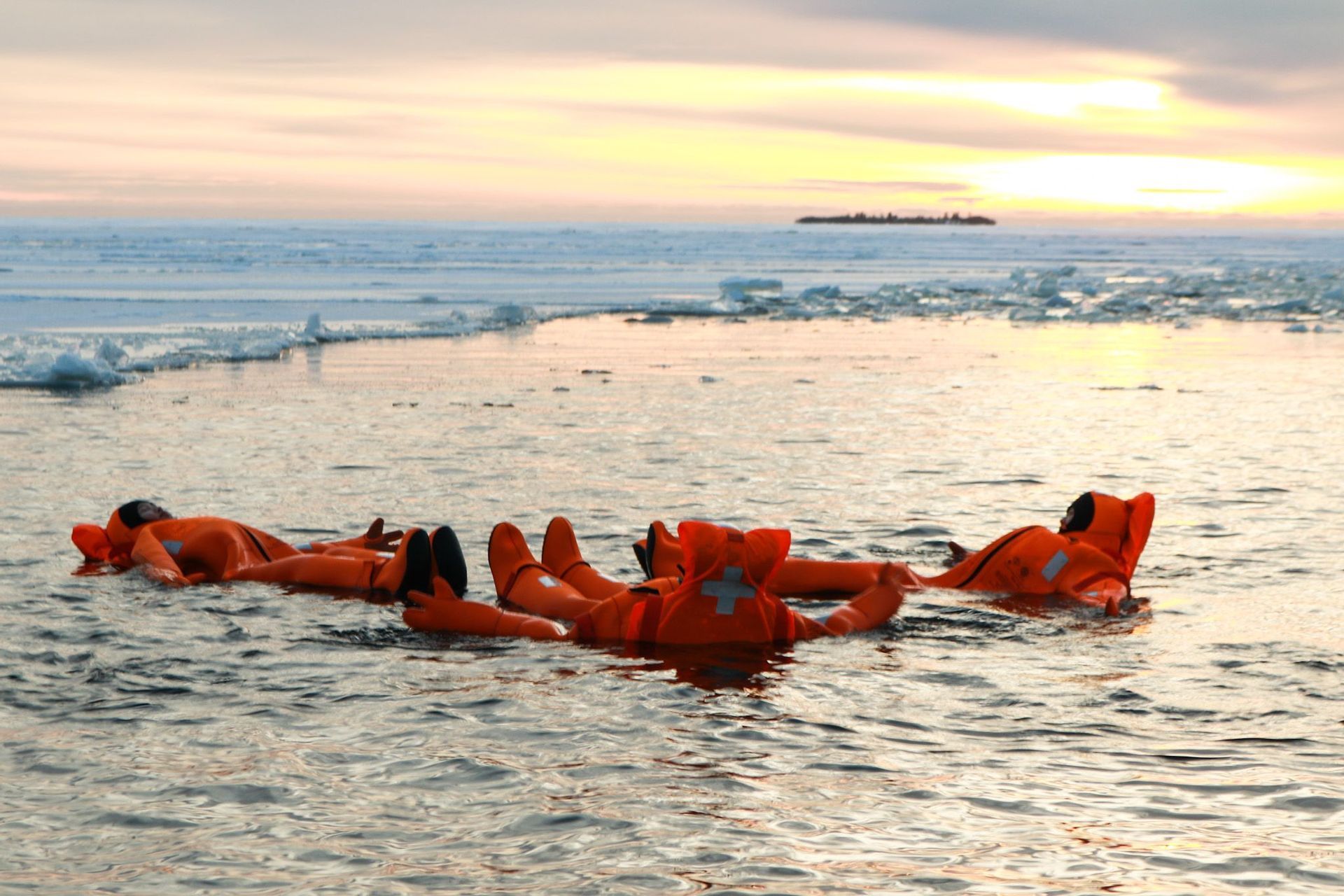 Un grupo de WeRoad flotando de espaldas en agua helada al atardecer, con trajes de inmersión naranjas.