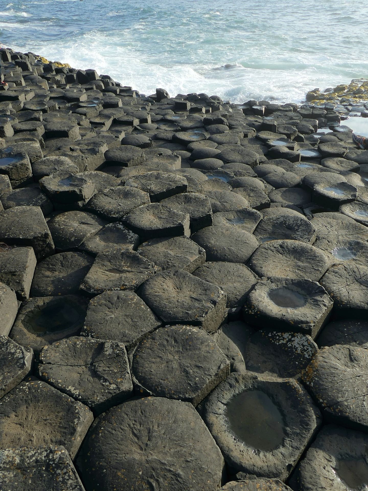 Colonne esagonali di basalto si incastrano a formare una pavimentazione naturale che incontra il mare agitato, con onde dalle creste bianche.
