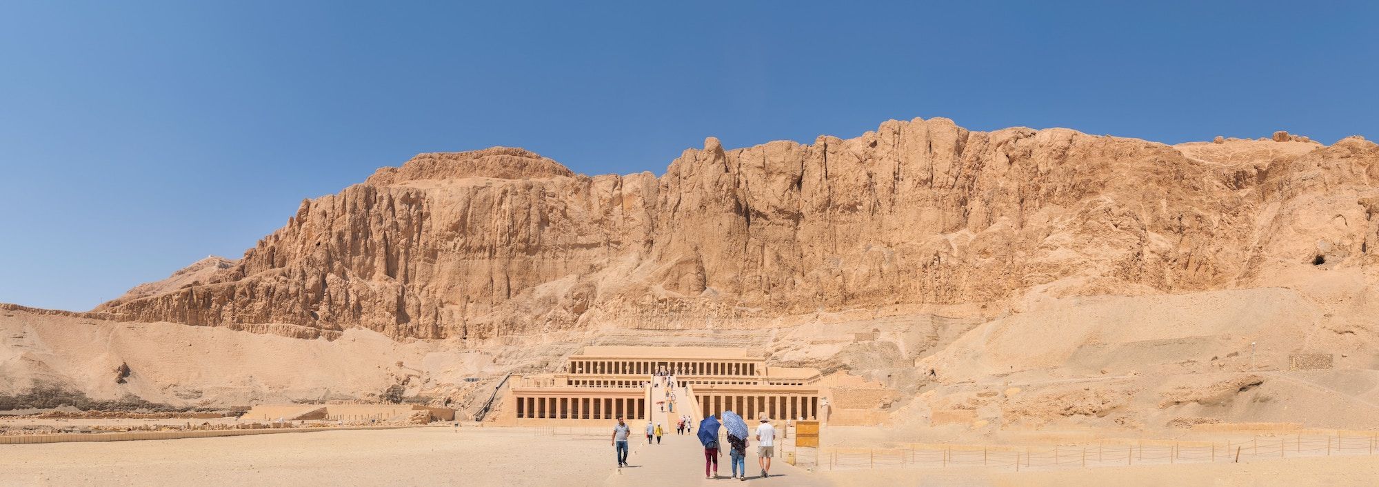 Un viaggio di gruppo WeRoad in cammino verso un grande tempio antico terrazzato, scavato nella base di una scogliera rocciosa nel deserto.