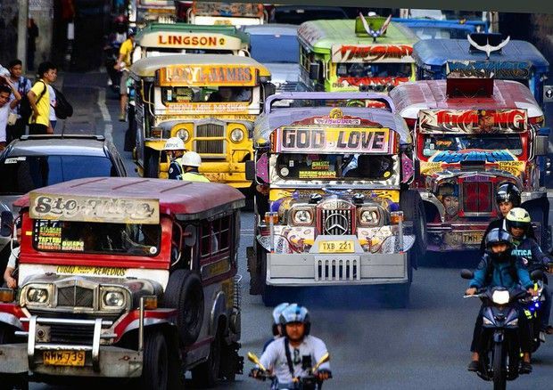 Diversi Jeepney colorati e motociclette percorrono una strada trafficata della città in mezzo al traffico intenso di giorno.