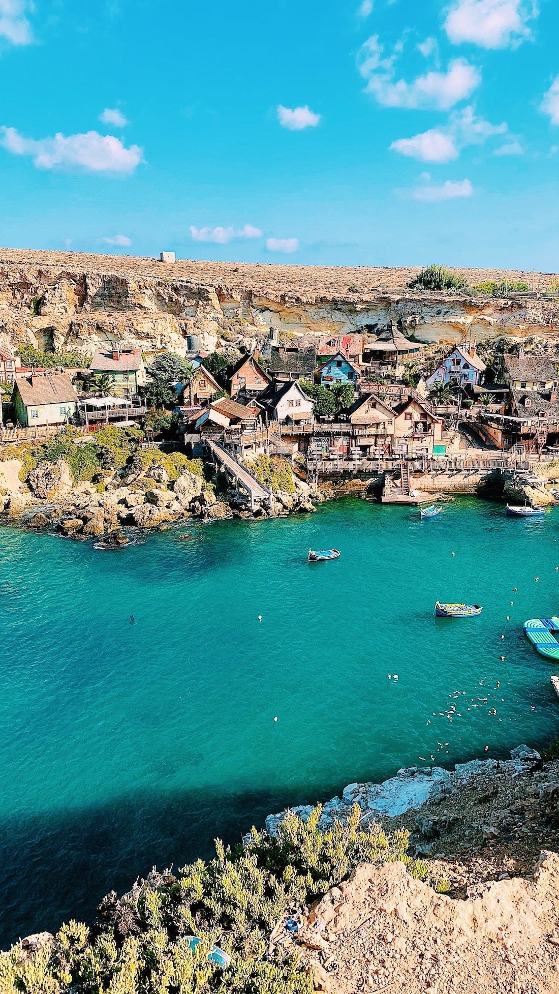 A colorful village built into a rocky cliffside, overlooking a small bay with turquoise water and several boats.