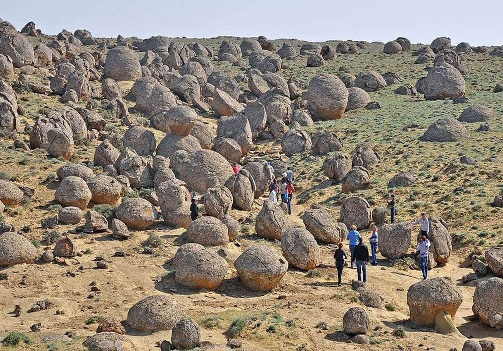 A WeRoad group trip walks on a path through a hilly landscape dotted with large, spherical rock formations under a clear sky.