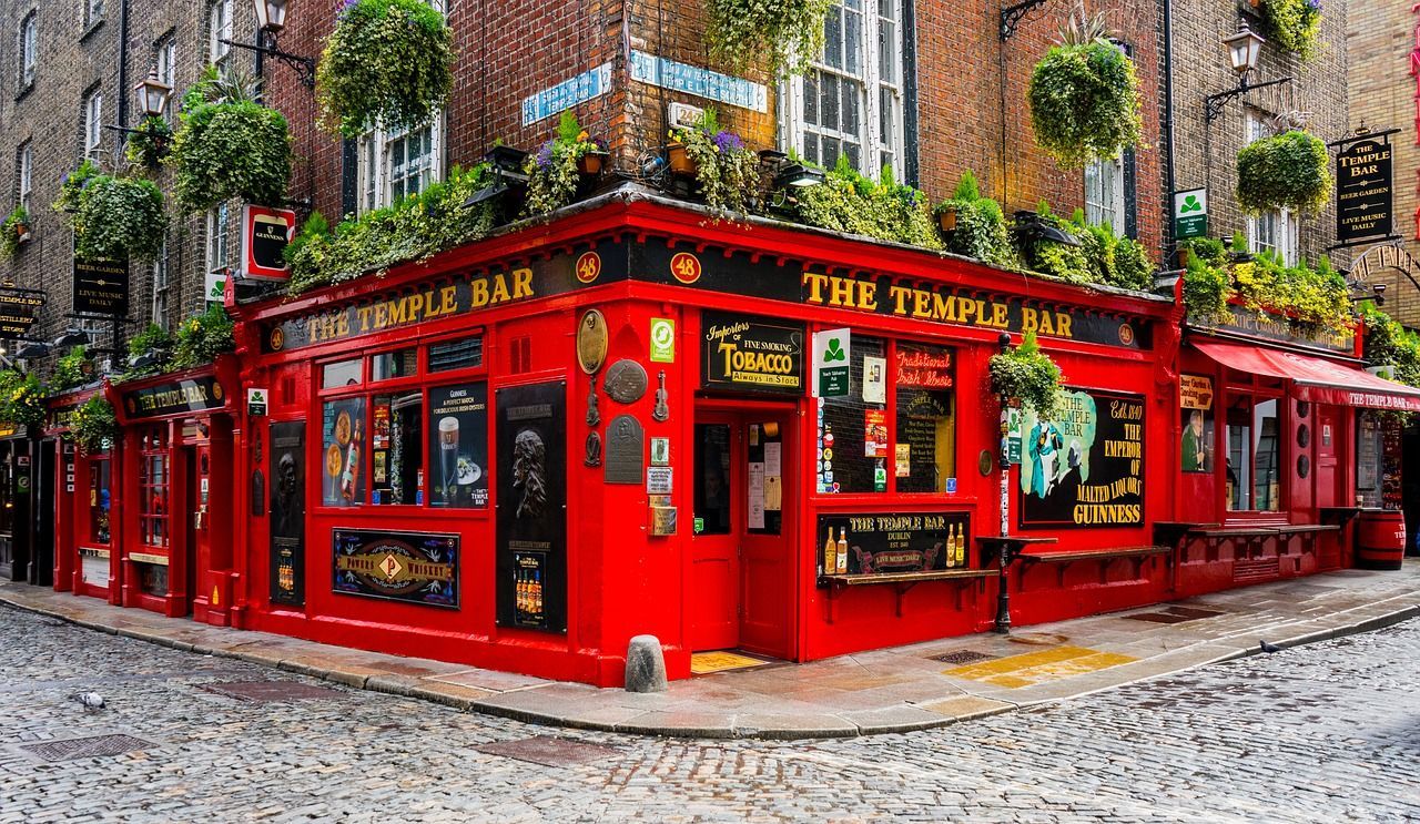 La facciata rosso vivo del pub The Temple Bar si erge su un angolo di strada acciottolata, decorata con piante verdi pendenti.
