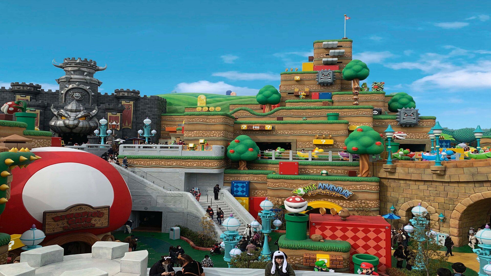 Un'ampia vista del parco a tema Super Mario World, con il Castello di Bowser e colline a più livelli punteggiate da elementi iconici del gioco.