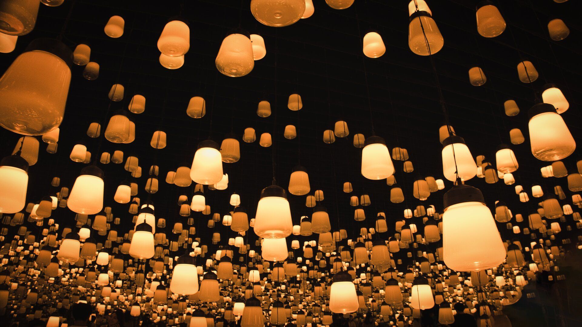 Una vista dal basso di innumerevoli lanterne arancioni luminose di varie dimensioni appese al soffitto in un ambiente buio.