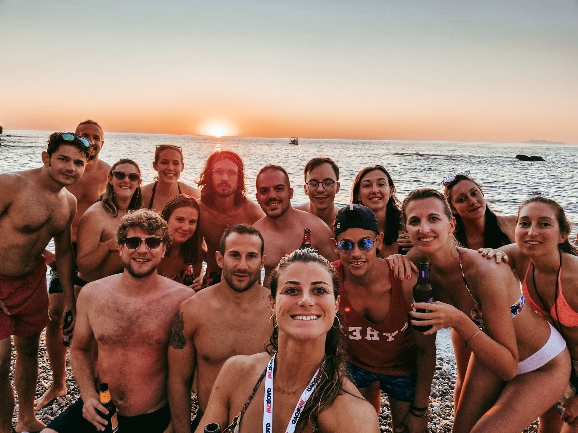 Un viaggio di gruppo WeRoad scatta un selfie su una spiaggia di ciottoli al tramonto sul mare.