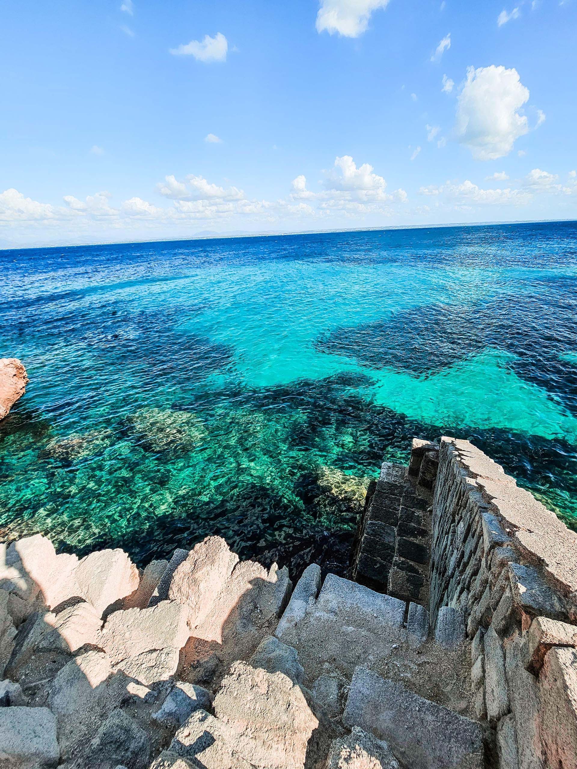 Una vista dall'alto di scale in pietra che scendono verso un mare turchese vibrante lungo una costa rocciosa.