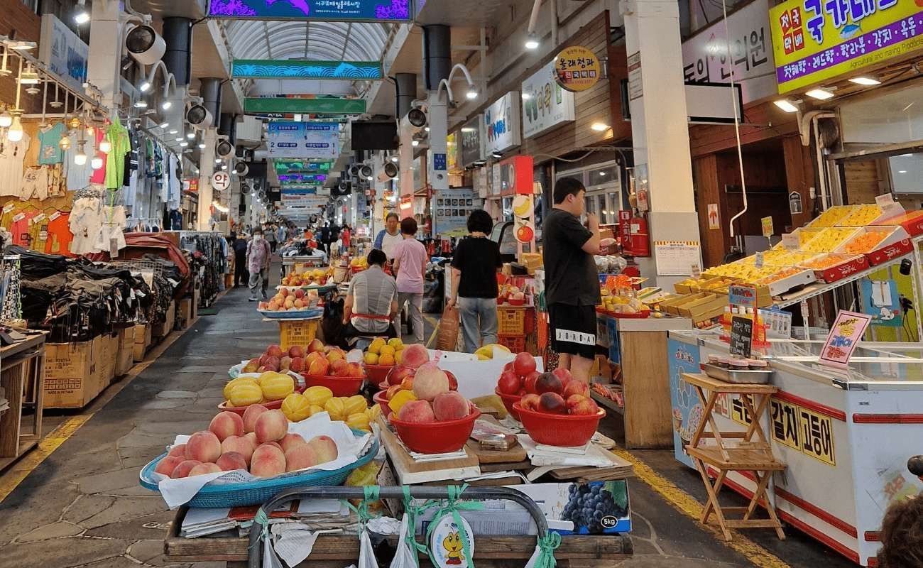 Vista su un vivace corridoio di un mercato coperto, con bancarelle che vendono frutta fresca come le pesche in primo piano.