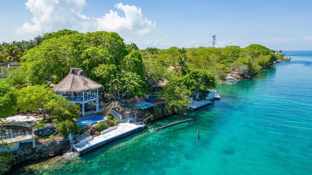 Vista aerea di un gazebo con tetto di paglia e di un resort su una costa lussureggiante e tropicale con acqua cristallina e turchese.