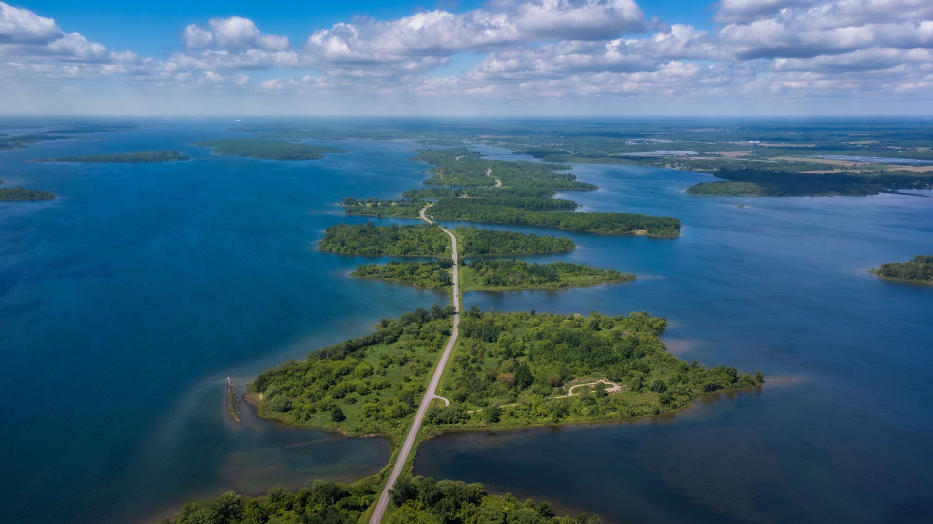 Vue aérienne d'une longue chaussée reliant une chaîne d'îles verdoyantes à travers une vaste étendue d'eau bleue.