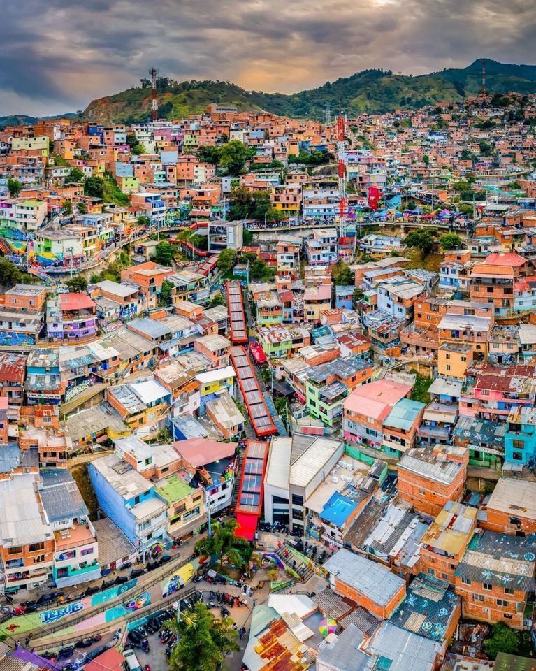 Una veduta aerea di scale mobili esterne rosse che salgono attraverso un quartiere colorato e densamente popolato, edificato su una ripida collina.