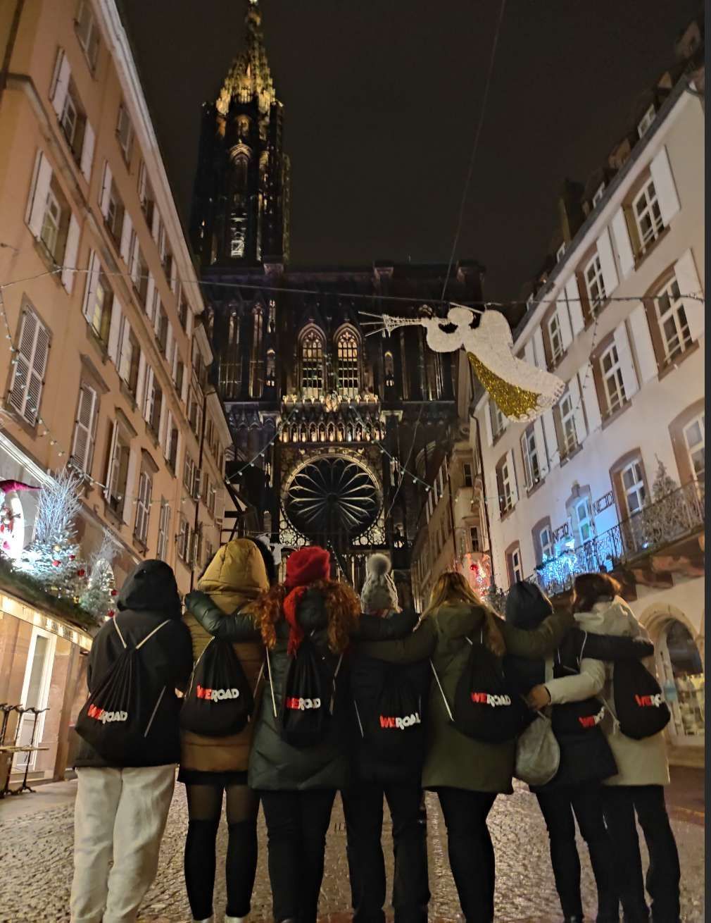 Eine WeRoad-Reisegruppe steht nachts auf einer Straße vor einer beleuchteten gotischen Kathedrale mit Weihnachtsdekoration.