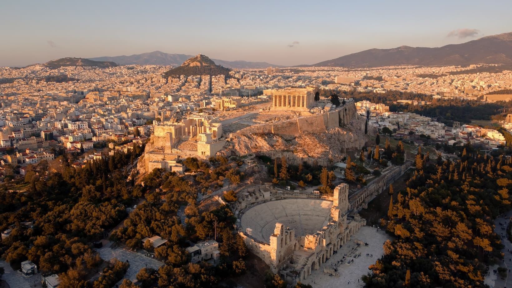 Veduta aerea dell'Acropoli e di un anfiteatro romano ad Atene, illuminati dalla luce dell'ora d'oro, che dominano il panorama cittadino.