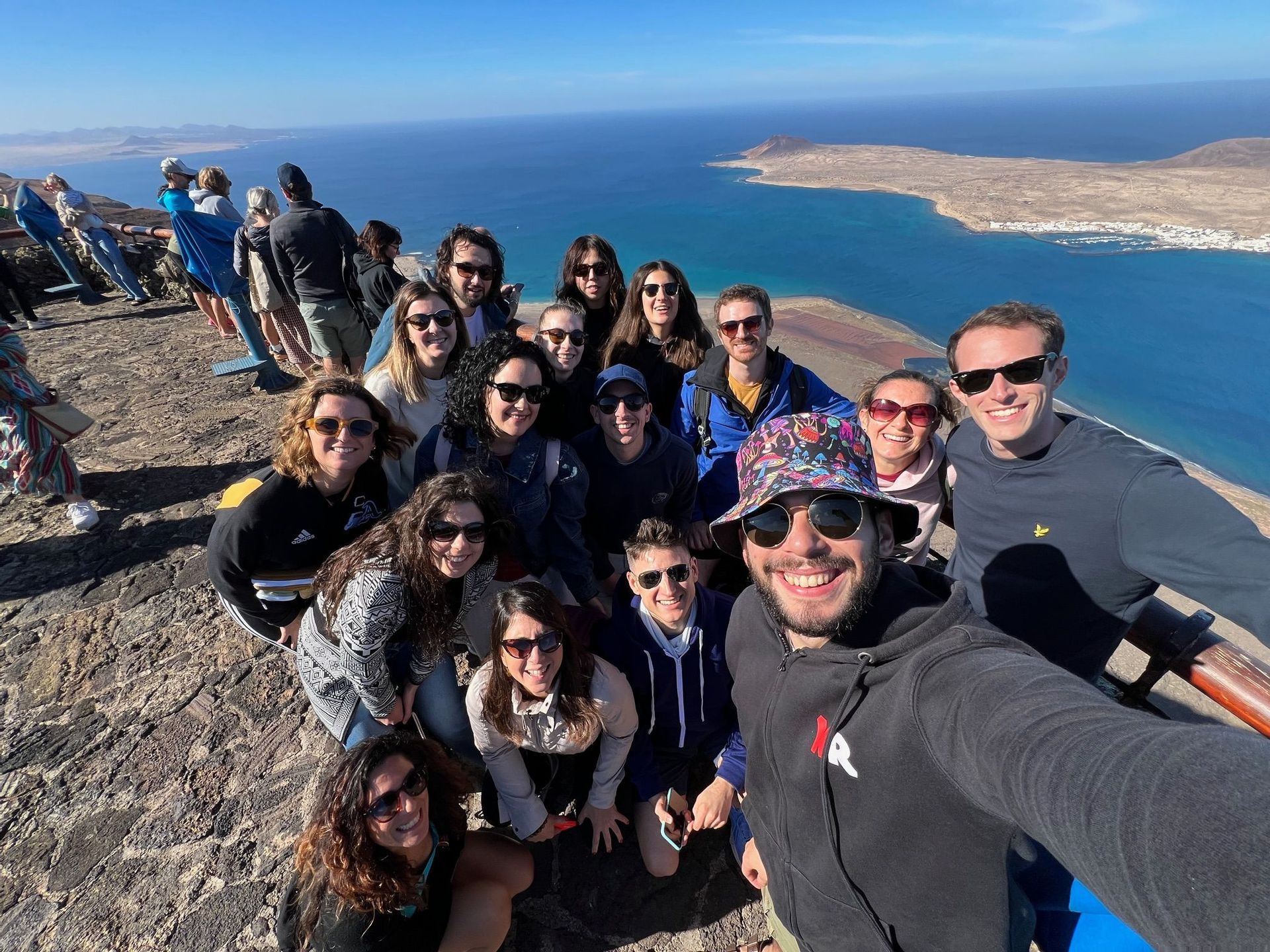 Un gruppo WeRoad si scatta un selfie da un punto panoramico elevato, con l'oceano blu e un'isola sullo sfondo.